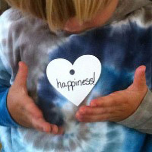 close up of girl with paper heart that reads “happiness”
