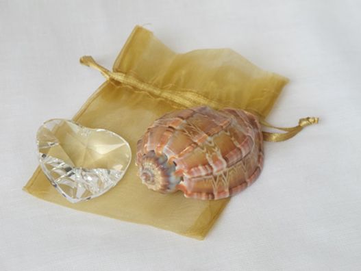 crystall heart and seashell sitting atop a sheer gold drawstring bag